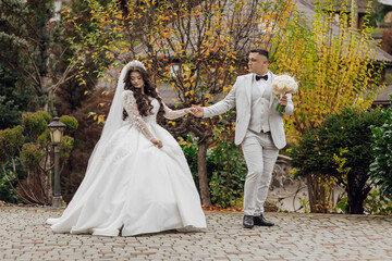 Wall Mural - A bride and groom are walking down a path in a park. The bride is wearing a white dress and the groom is wearing a suit. They are holding hands and appear to be happy and in love