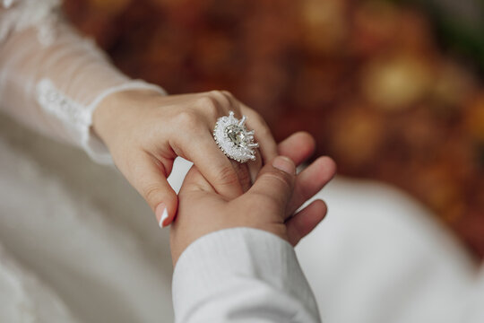 a couple is holding hands and the woman is wearing a ring. the ring is large and has a diamond in th