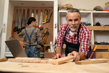 Senior Carpenter man working with his co-worker in furniture , working with piece of wood and tablet.