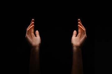 This image shows two hands reaching upward in the dark. The hands are positioned symmetrically, with their palms facing upwards.