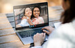 © Prostock-studio - A woman sits outdoors at a wooden table and uses her laptop to video chat with two girlfriends. The woman on the laptop is smiling and appears to be happy to be talking to her friends.