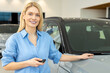 © zinkevych - Blonde cute woman standing near the car in a car salon and looking excited