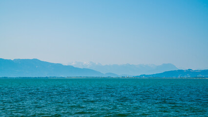 Germany, Snow covered mountains nature landscape behind water of bodensee lake, panorama view from lindau to swiss and austrian coast on misty day