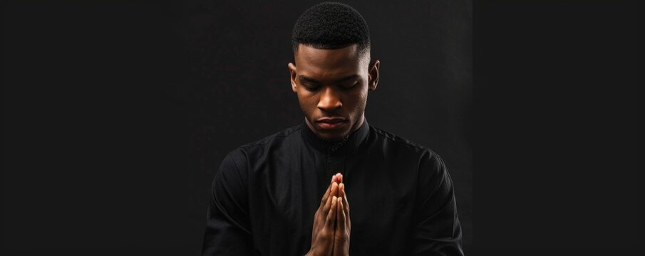 Black man praying with folded hands isolated on a black background.
