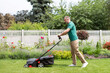 © Home-stock - Side view of man using lawn mower cutting the grass in the backyard. Modern agricultural machinery for the care of the garden