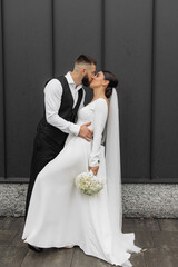 Wall Mural - A bride and groom are kissing in front of a building. The bride is holding a bouquet of flowers