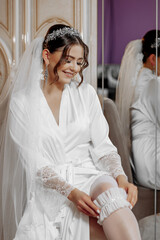 Wall Mural - A bride is sitting in a white robe and wearing a veil. She is smiling and she is happy