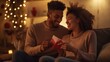 © nopommajun - A couple sitting on a couch exchanging cards in a cozy holiday setting with twinkling lights and festive decorations in the background.