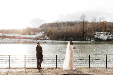 Wall Mural - A bride and groom stand on a pier overlooking a body of water. The bride is holding a bouquet and the groom is holding a bottle. The scene is serene and romantic