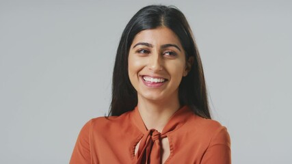 Wall Mural - Head and shoulders studio portrait of smiling young Indian businesswoman against grey background wearing business suit looking off camera - shot in slow motion