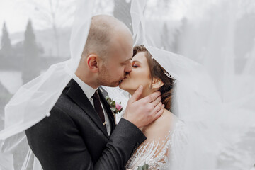 Wall Mural - A man and woman are kissing under a white veil. The bride is wearing a white dress and the groom is wearing a black suit. The scene is intimate and romantic, capturing the love