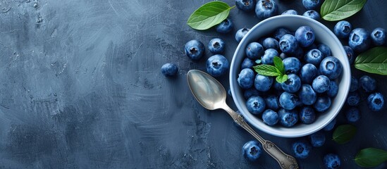 Poster - Bowl with fresh organic blueberries, leaves, and a spoon on a grey backdrop with copy space image.