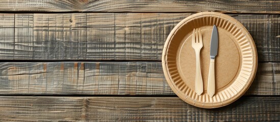 Poster - Empty brown paper plate and fork with knife on a wooden table. View from above. Eco-friendly disposable tableware. copyspace. Copy space image. Place for adding text or design