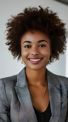 Wall Mural - A woman with a short, curly hairstyle is smiling and wearing a gray suit jacket. She is posing for a photo, and her expression conveys a sense of confidence and positivity