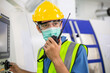 © winnievinzence - Male worker wearing medical mask talking on walkie-talkie with colleague to control work in front of technology machine at industrial plant factory. copy space