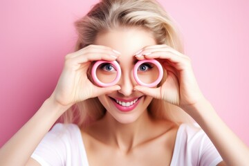 Wall Mural - A woman is holding pink eye glasses and smiling. The image conveys a playful and lighthearted mood, as the woman is posing with the glasses as if she is looking through them