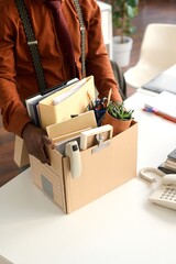 Vertical closeup of person holding box with personal items at workplace table and unpacking for new job