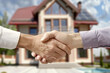© Renata Hamuda - Close up of handshake between a real estate agent and a client, new property in the background