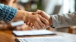 © NDmCX-Nic - Close-up of two people shaking hands over a table with paperwork.  A symbol of agreement, partnership, and success.