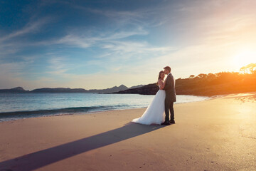 Wall Mural - Bride and groom on a beach at sunset