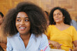 © Altura - Young latin female university student with afro hairstyle smiling sitting in classroom.
