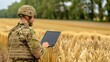 © lililia - A soldier in camouflage uniform stands in a wheat field and uses a laptop computer