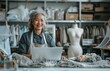 © yevgeniya131988 - Senior Asian fashion designer working at her desk with a laptop and tablet, surrounded by mannequins and boxes