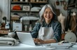 © yevgeniya131988 - Senior Asian fashion designer working at her desk with a laptop and tablet, surrounded by mannequins and boxes
