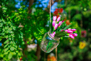 A vase with pink flowers hanging from a tree branch