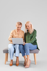 Wall Mural - Beautiful mature women with laptop sitting on bench against grey background