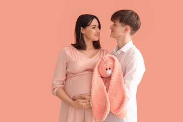 Poster - Young pregnant couple with toy bunny on pink background