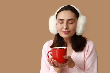 Wall Mural - Beautiful young woman with cup of hot mulled wine on brown background
