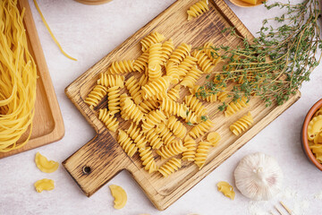 Poster - Wooden board with uncooked fusilli pasta and thyme on light background
