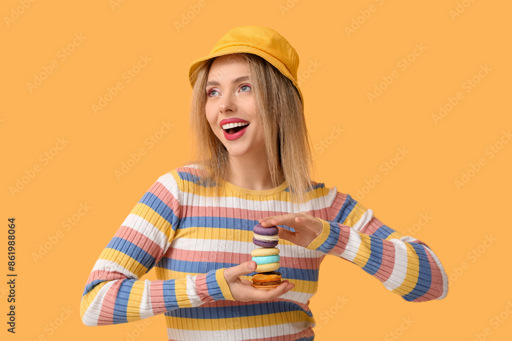 Happy young woman with different sweet macaroons on yellow background