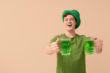 Wall Mural - Happy young man in leprechaun's hat with mugs of beer on beige background. St. Patrick's Day celebration