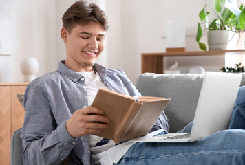 Wall Mural - Male student with book studying online on sofa at home