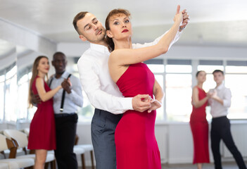 Wall Mural - With unhurried music, guy and woman in couple spins to rhythm of waltz during lesson for novice students. Classes in mini-groups for those who want to learn dancing