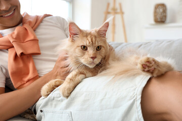 Wall Mural - Handsome young happy man with cute Maine Coon cat lying on sofa at home, closeup