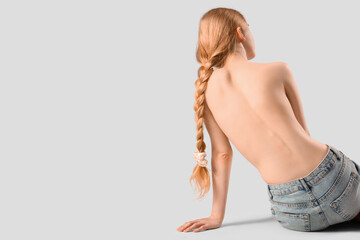 Wall Mural - Beautiful young woman with naked back sitting on grey background