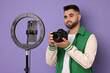 © New Africa - Technology blogger reviewing camera and recording video with smartphone and ring lamp on purple background