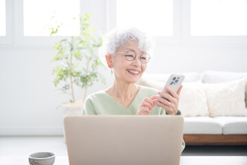 Wall Mural - tapping smiling senior (elderly) woman with computer and smartphone (smart phone) tapping and operat