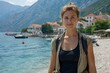 © naphat - A young woman in her thirties, wearing black tank top and brown long skirt with jacket is standing on the shore of Konia Bay near Perast town behind mountains. She has short blonde hair tied back and