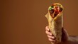 © Sweettymojidesign - A burrito gripped by a hand, against a solid brown backdrop with copy space