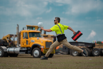 Wall Mural - Hispanic 40 s builder excited jump on site construction. Excited builder construction worker in a safety helmet jumping in front of the trucks. Excited crazy builder man in helmet jump outdoor.