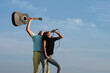 © Volodymyr - Excited young couple enjoy music, move emotionally. Two carefree overjoyed people dancing and singing outdoor. Photo of crazy carefree couple sing hold mic and guitar. Crazy song.