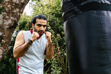 Colombian man with long hair exercising with punching bag outdoors. Kick boxing, boxing, martial arts