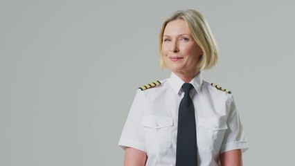 Sticker - Smiling mature female airline pilot or ship captain wearing uniform turning to face camera in front of plain studio background - shot in slow motion