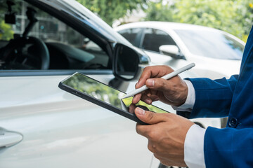 a businessman stands next to his damaged vehicle after an accident, holding a clipboard and examinin