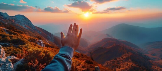 Wall Mural - Hand reaching towards the sun in a golden sunset over mountains. Concept of hope, dreams, achievement and success.