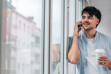 Wall Mural - young man with mobile phone and cup at home window